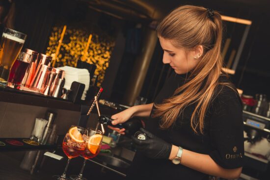 Bartender pouring a cocktail with orange garnish.