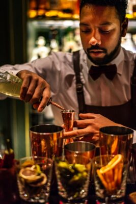 Bartender measuring and pouring a cocktail behind the bar.