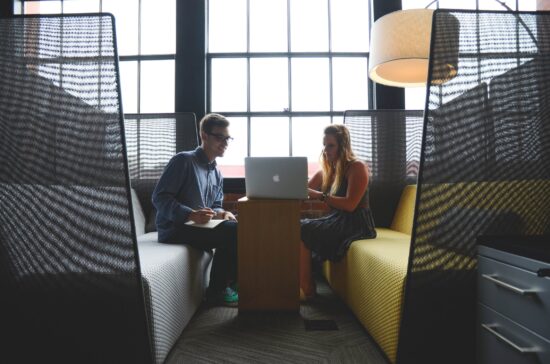 Two people working together on a laptop in an office booth.