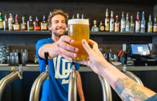 Bartender handing a beer to a customer at the bar.