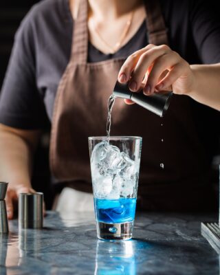 Bartender pouring liquid into a glass with ice.