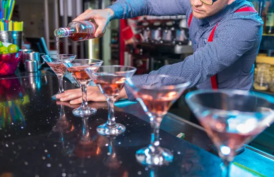 Bartender pouring drinks into multiple cocktail glasses.