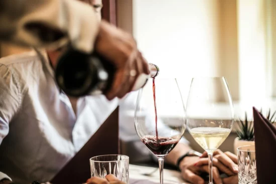 Person pouring red wine into a glass at a table.