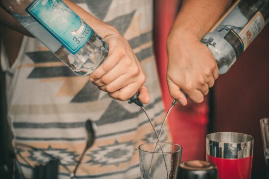 Bartender pouring liquor into a glass with a jigger.
