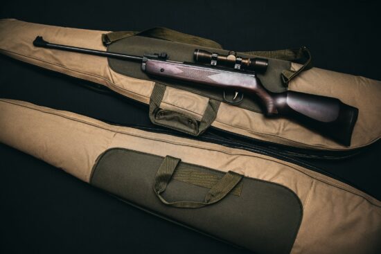 Rifle with scope resting on a carrying case.