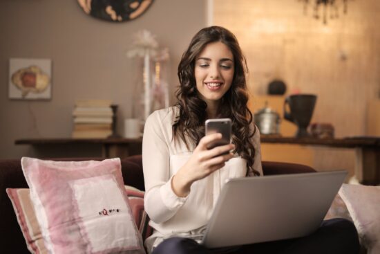 Woman using a phone and laptop while sitting on a couch.