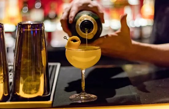 Bartender pouring a cocktail into a glass with garnish.