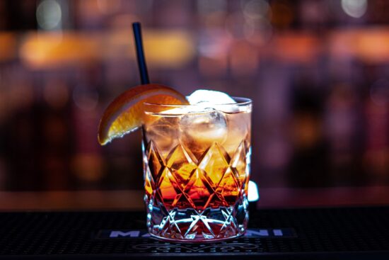 Old fashioned cocktail with orange slice on a bar.
