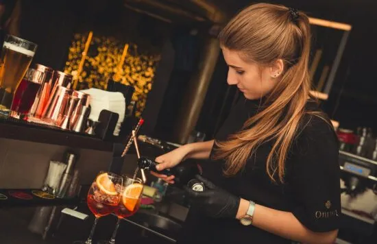 Bartender pouring a cocktail with orange garnish.