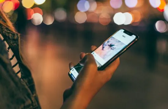 Person using a smartphone at night with blurred lights.