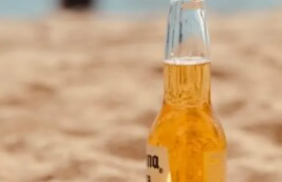 Beer bottle with a lime on a sandy beach.