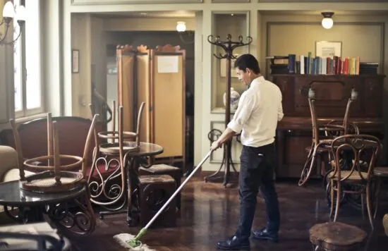 Worker mopping the floor in an empty restaurant.