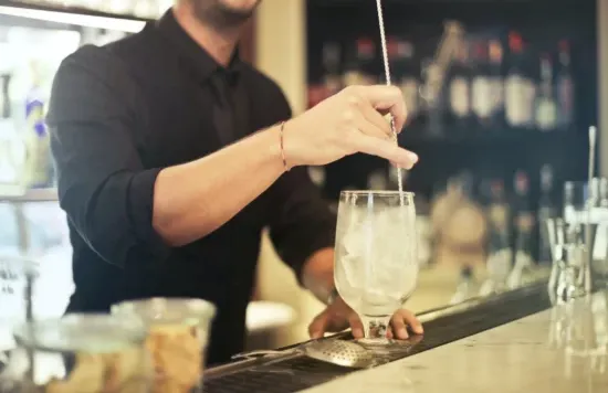Bartender stirring a drink with ice in a glass.