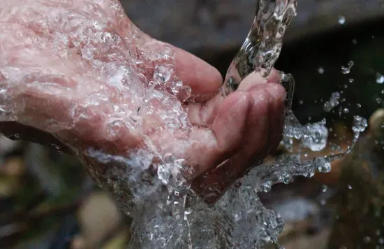 Hands catching running water from a stream.