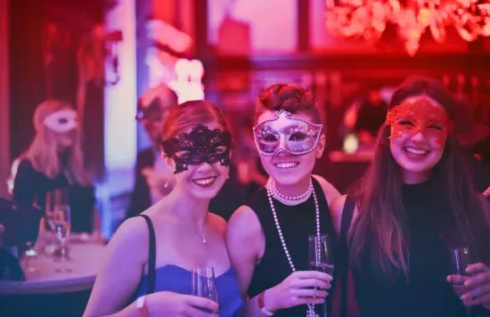 Group of women wearing masks and holding drinks at a party.