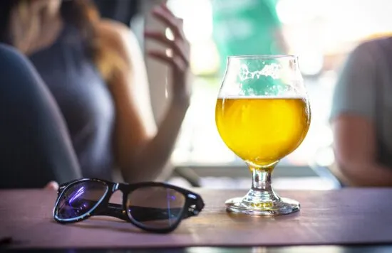 Glass of beer on a table with sunglasses nearby.