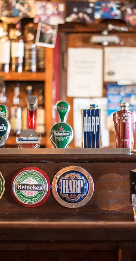 Beer taps on a bar counter with bottles in the background.
